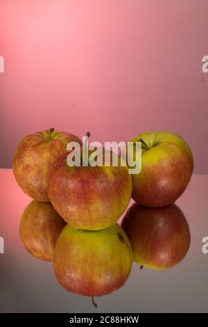 Three red apples on mirroring table on mirror red background with reflection isolated close up Stock Photo
