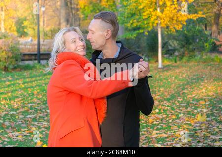 Middle-aged couple having fun in autumn park. Dancing couple on fall trees background. Man and woman hugging on colorful park. Happy family in nature Stock Photo