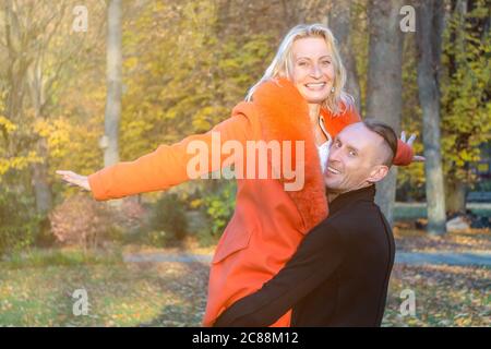 Middle-aged couple in autumn park. Smiling man holding woman in hands on colorful fall background. Happy couple on fall trees background.Pair Stock Photo