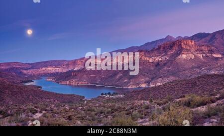 Moon setting down at sunrise over Apache Lake in Superstition Mountains, view from Apache Trail, Arizona, USA Stock Photo