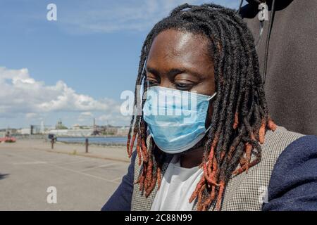 A young African man wears a medical mask to protect himself from the coronavirus outbreak. Close-up . A man in a wheelchair. Summer sunny day. High quality photo Stock Photo
