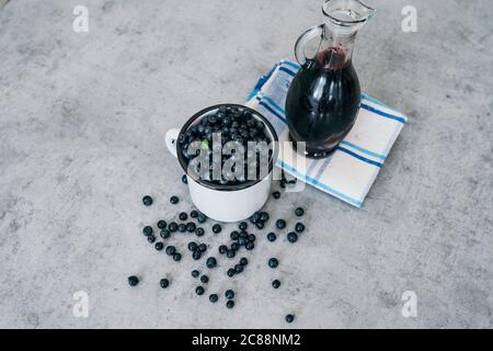 Fresh blueberry with drops of water in white cup. Blueberry syrup in glass bottle or mixture, on wooden background. Stock Photo