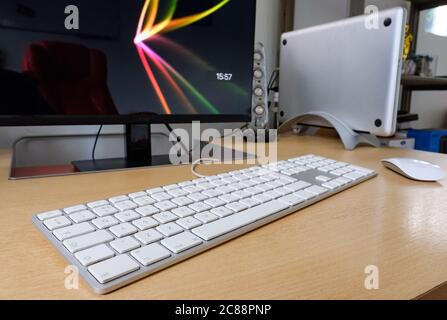 Detailed view of a cradled laptop computer used on a office desk with an extended keyboard, wireless mouse and computer monitor in use. Stock Photo