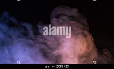 Conceptual image of multi-colored smoke isolated on dark black background and wooden table. Stock Photo