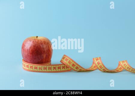 Ripe red apple and yellow measuring tape curles on a blue medical background. Concept of healthy eating, body weight control, weight loss and slimming Stock Photo
