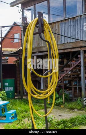 yellow garden hose hanging from a metal pole in the backyard Stock Photo