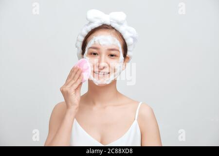 Happy young Asian woman applying foaming cleanser on her face and wearing towel on her head. Stock Photo