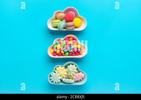 sweets - lollipop, meringues, macaroon in bowl in shape of cloud, chocolate, with colorful topping donut isolated on blue background Flat lay Top View Stock Photo
