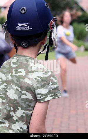 Child in cricket gear from behind playing cricket practice at home in UK garden during lockdown, 2020 Stock Photo