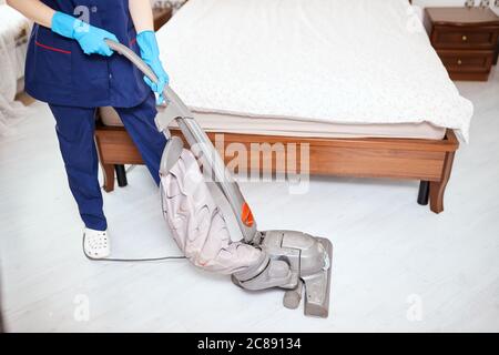 Close up of hotel maid cleaning the white carpet with vacuume cleaner. Cleaning Service concept. Stock Photo