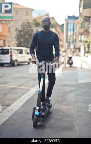 Young stylish African male with glasses riding a scooter under the sunlight at daytime Stock Photo