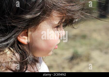 Profile and close-up portrait of gorgeous little girl with fluttering long hair on a blurry outdoors background Stock Photo