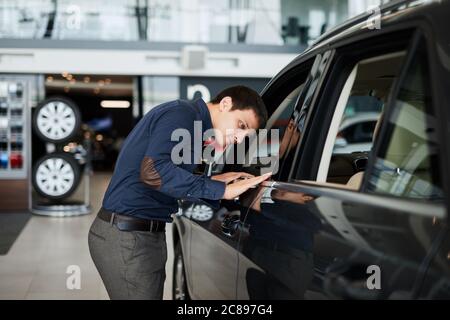 Professional salesman checking out interior and design of a new car at the dealership car, dealer helping his customer to buy luxury vehicle Stock Photo