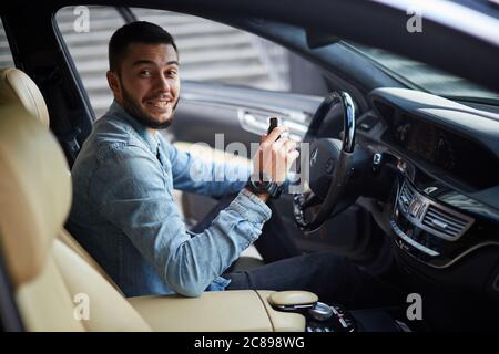 happy joyful guy is holding flash drive while sitting in the vehicle. side view photo Stock Photo