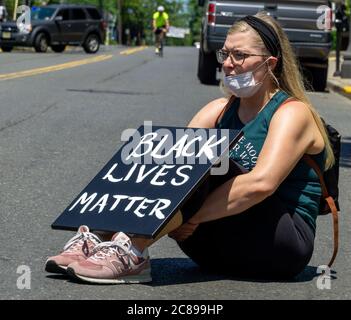 Black Lives Matter Protest in Ridgefield Park, New Jersey white girl holding BLM sign sitting in street Stock Photo