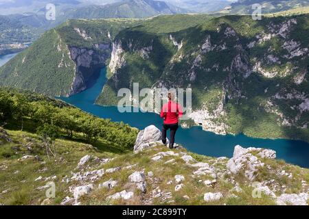 Woman in red jacket standing on the mountain with view on Pivsko lake in Montenegro, Europe Stock Photo