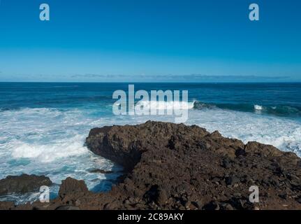 Volcanic rock formation, cliffs of black lava on the rocky shore with crushing white waves over the Atlantic Ocean. Blue sky background. La Palma Stock Photo