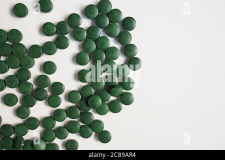 Green pills on wooden scoop isolated on white background with reflection. Spirulina, chlorella and wheatgrass. Healthy living concept. Stock Photo