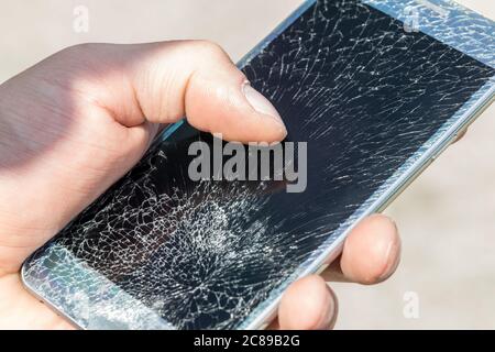 A young man is holding a phone with a very cracked touch screen Stock Photo