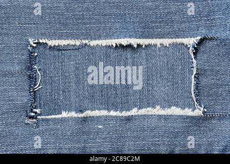 torn piece of denim in oblong shape on denim surface for messages Stock Photo