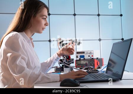 A young woman writes an algorithm for the robot arm. Science Research Laboratory for Robotic Arm Model. Computer Laboratory Stock Photo