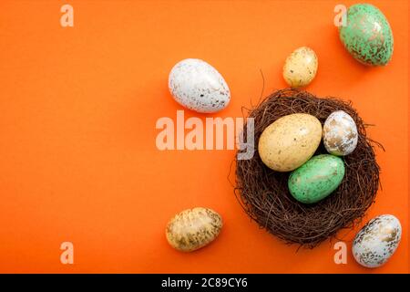 Happy easter and spring meme concept with a colorful image of easter eggs dyed white, green and yellow with gold spots in bird nest against a orange b Stock Photo