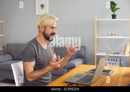 Man businessman wearing glasses in casual clothes working talking video call chat having laptop while sitting at a table in the apartment. Stock Photo