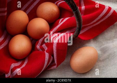 Natural ingredients, healthy food and rustic setting concept with a wicker basket covered with a vintage red cloth flipped on one side with eggs insid Stock Photo