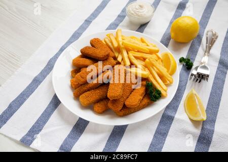 Homemade Fish Sticks and French Fries with Tartar Sauce on a white wooden background, low angle view. Stock Photo