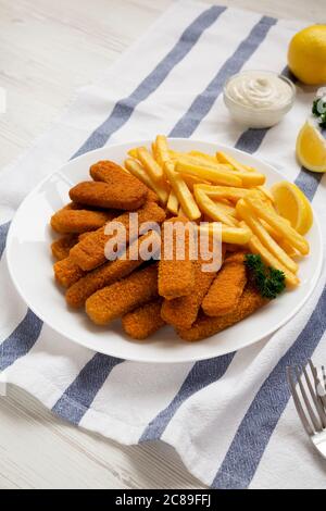 Homemade Fish Sticks and French Fries with Tartar Sauce on a white wooden background, low angle view. Stock Photo