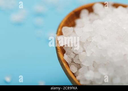 In a wooden spoon, sea salt crystals on a blue background, macro. Stock Photo