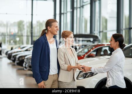 Professional caucasian young female salesperson working in car dealership, conculting potential clients about car purchase loans Stock Photo