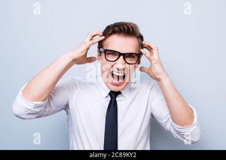 Going crazy and insane. Close up portrait of shouting stressed young entrepreneur in a formal wear and glasses, standing on pure light background Stock Photo