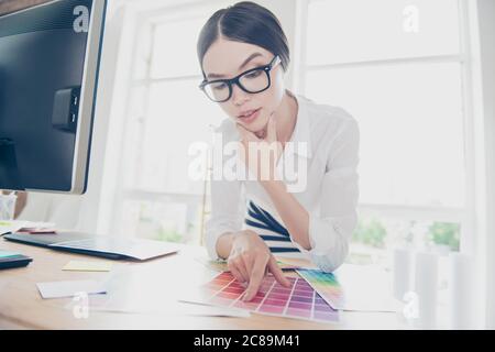 Pensive attractive asian interior designer, architect, stylist, choosing the colors for new project, pointing at the sample, wearing smart outfit, spe Stock Photo