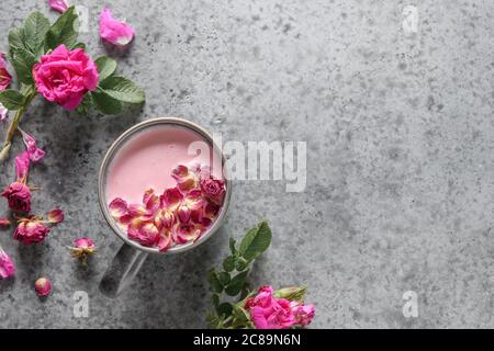 Rose moon milk in grey cup and rose petals on grey. Top view. Stock Photo