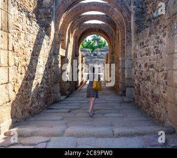 Woman with her back advancing through a stone corridor towards the Roman Amphitheater in Mérida, as if she were an actress or dancer who goes on stage Stock Photo