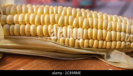 Part of a raw corn on the cob on a wooden board with natural light outdoors Stock Photo