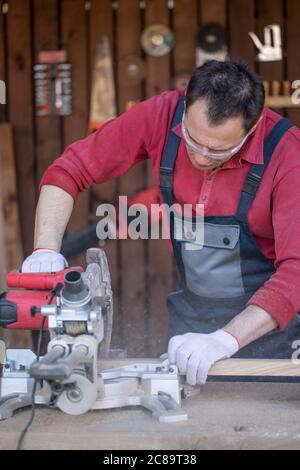 Caucasian man in protective overalls cuts wooden oak plank with a circular saw Stock Photo