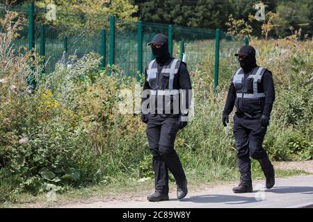 Harefield, UK. 22 July, 2020. Masked HS2 security guards walk along Harvil Road to a site for the HS2 high-speed rail link which had been occupied by activists from HS2 Rebellion in order to hinder tree felling works. Environmental activists continue to protest against HS2, which is currently projected to cost £106bn and will remain a net contributor to CO2 emissions during its projected 120-year lifespan, from a series of wildlife protection camps along its route. Credit: Mark Kerrison/Alamy Live News Stock Photo