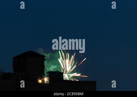 a fireworks explosion on a new york city rooftop, pink and green light and smoke flash from the rooftop against a dark blue night sky with copy Stock Photo