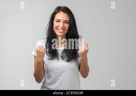 positive cheerful girl celebrating the victory. close up photo. isolated on the gray background. awesome girl achieved the goal. copy space. beautiful