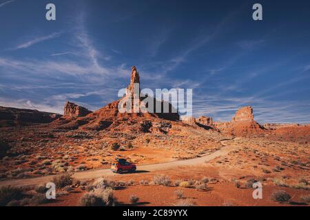 An orange car is driving through the Valley of Gods, Utah Stock Photo