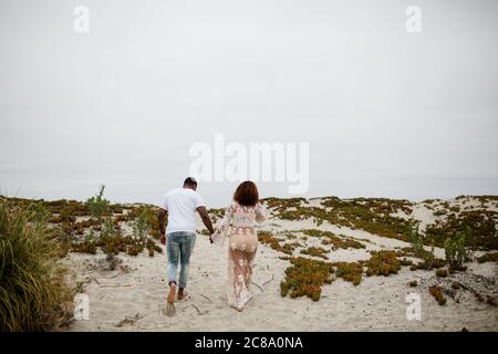 Mixed Race Couple Holding Hands Walking on Beach Stock Photo