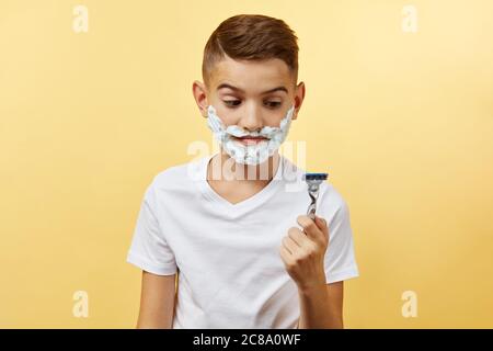 shoking boy do not know how shaving with razor blade in his hand, on yellow background Stock Photo