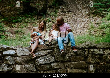 Happy young diverse family sitting on rocks in forest smiling Stock Photo