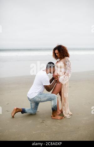 Mixed Race Couple on Beach, Kissing Baby Belly Stock Photo