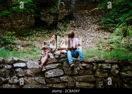 Happy multiracial family laughing while sitting on rocks in forest Stock Photo