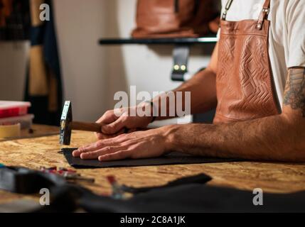 craftsman working with hands and hammer on leather in laboratory Stock Photo