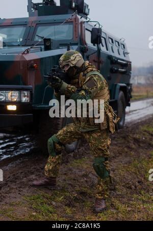 a soldier moves undercover with an armored car on the side of a road in the rain Stock Photo