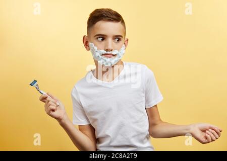 shoking boy do not know how shaving with razor blade in his hand, on yellow background Stock Photo